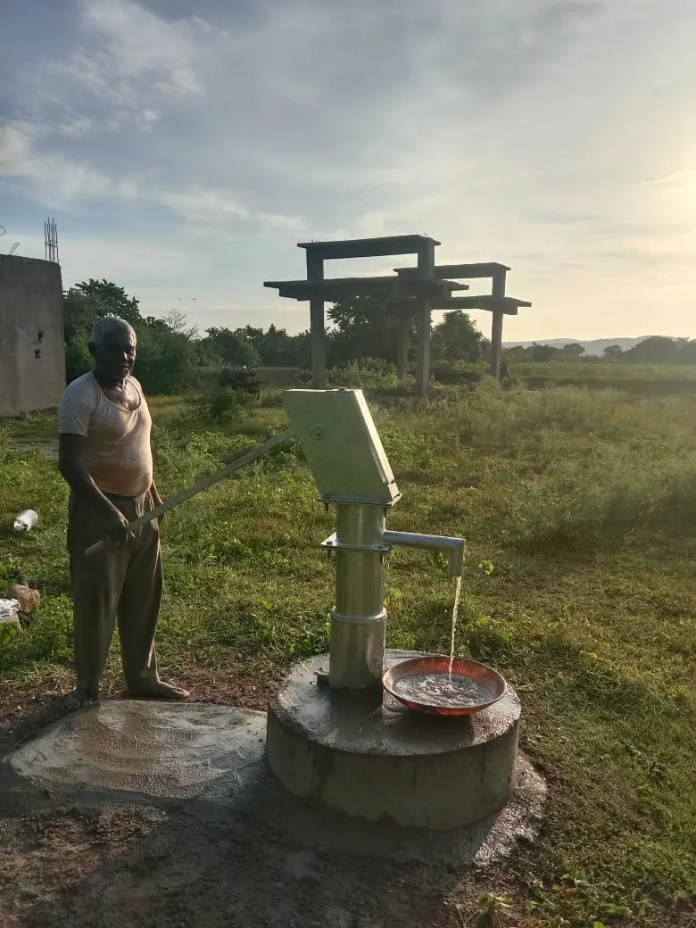 Villager at a newly installed borewell hand pump, water flowing into a basin